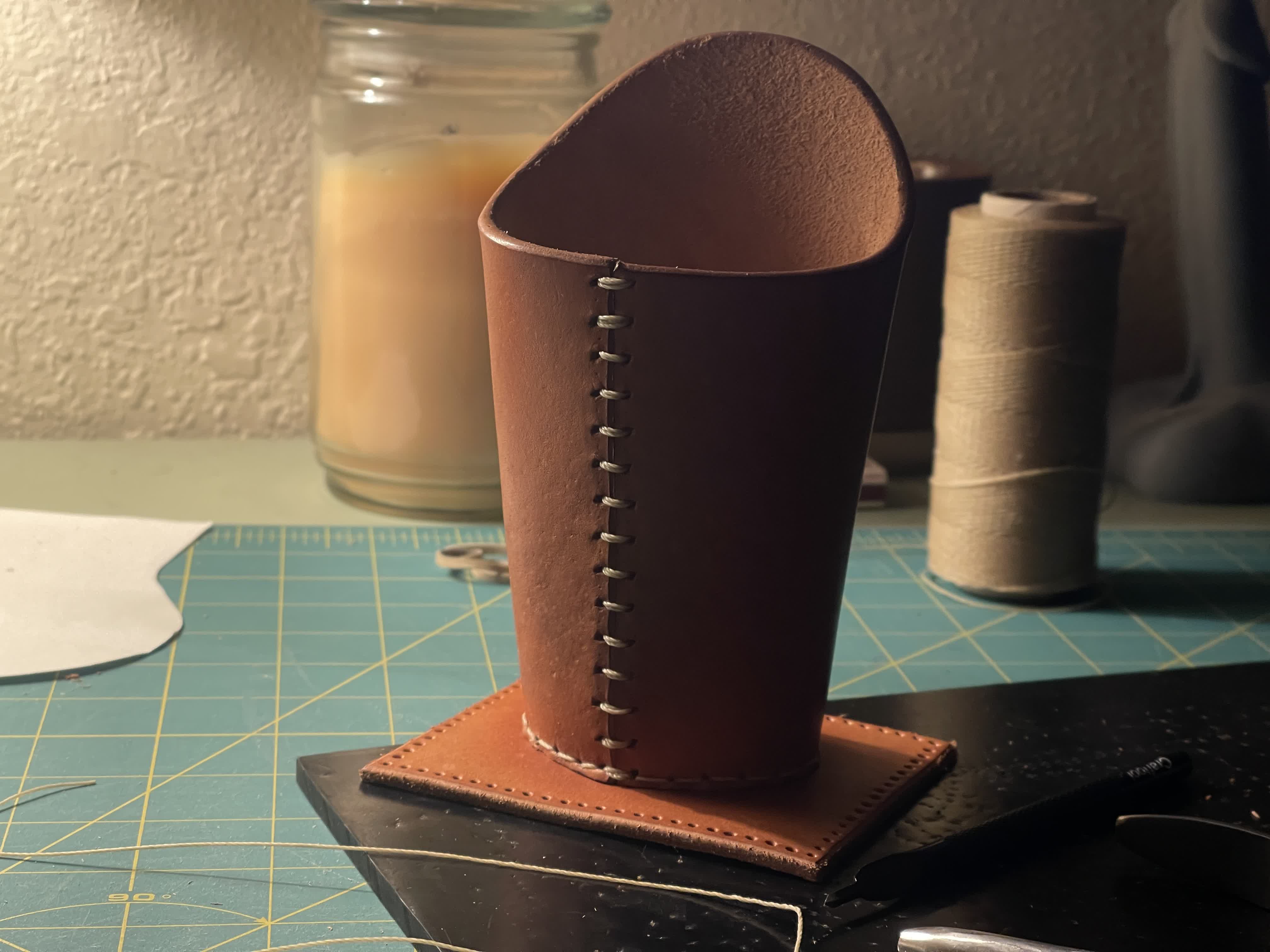 Tooled leather eyeglass holder standing upright on a work table.